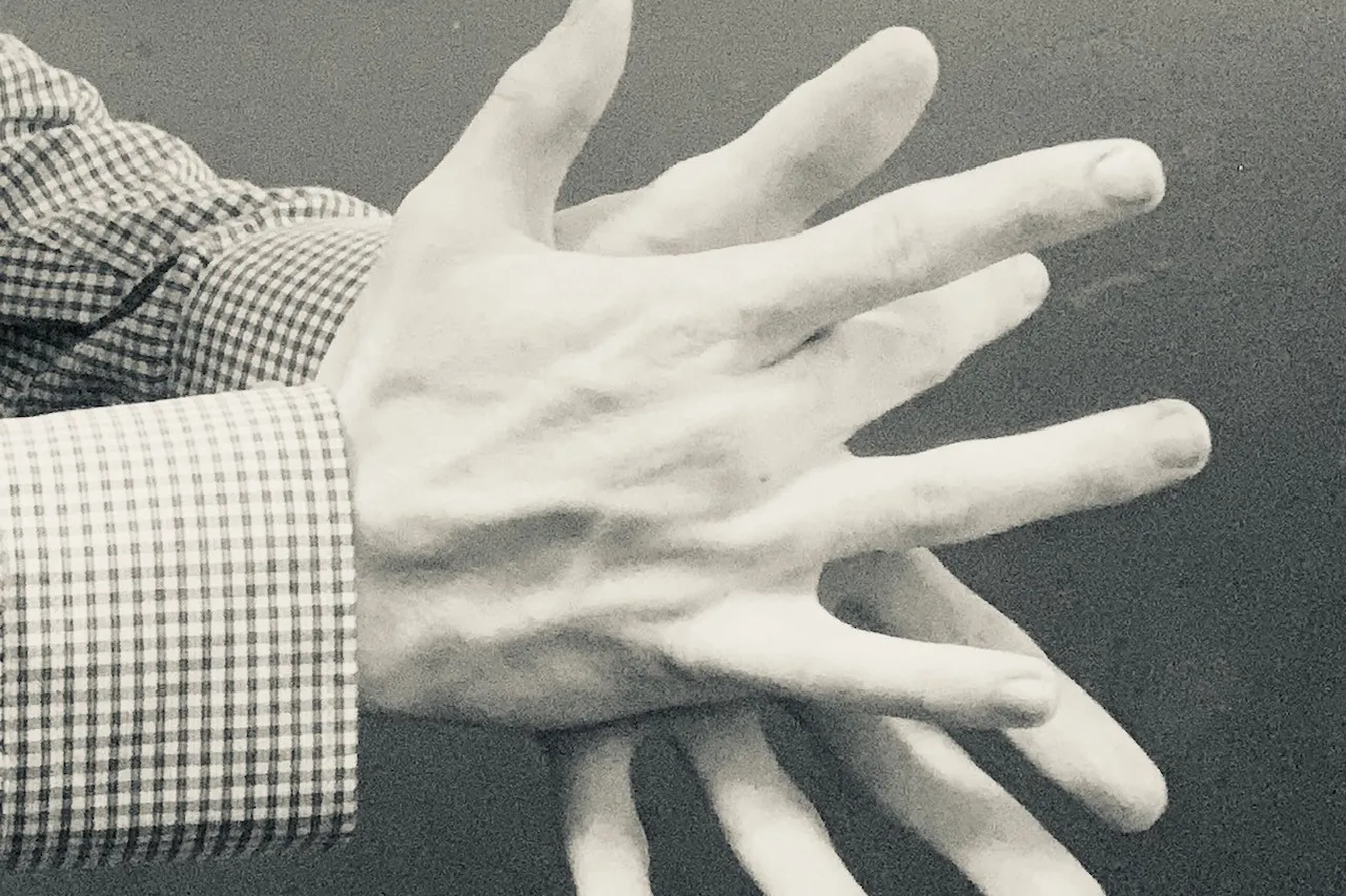 A pair of hands clapping, seen from the side against a grey background, the fingers spread