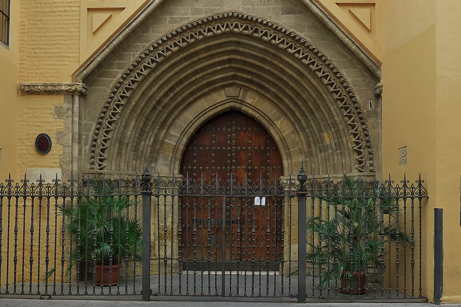 The Gothic-Mudéjar doorway of the Church of Santa Ana in Triana, with a carved arch above a wooden door and iron railings in front